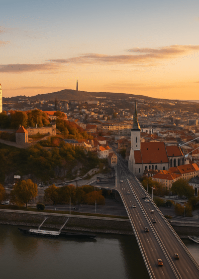 Edessä näkyy pitkä silta, joka menee joen yitse. Sillan takana näkyy paljon punakattoisia taloja. Vasemmalla kukkulan päällä on linna.