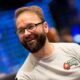 Kuvassa on kanadalainen pokeriammattilainen Daniel Negreanu, yksi maailman tunnetuimmista ja menestyneimmistä pelaajista. Hän hymyilee iloisesti ja rennosti katsellen sivuun. Negreanulla on yllään vaaleanharmaa pitkähihainen paita, jonka rinnassa on hänen pitkäaikaisen sponsorinsa PokerStarsin logo. Hänellä on myös tunnusomaiset silmälasit ja siististi hoidettu parta. Tausta on epätarkka (bokeh-efekti), ja siinä näkyy lukuisia sinisiä valopisteitä, mikä luo kuvaan dynaamisen ja suuren turnaustapahtuman tunnelman. Valokuvan on ottanut Danny Maxwell.