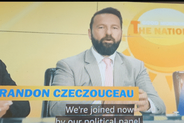 Kuvassa näkyy televisiostudion keskustelupaneeli, jossa kolme henkilöä istuu vierekkäin kirkkaankeltaista taustaa vasten. Keskimmäinen mies puhuu kameralle, pukeutuneena vaaleaan pukuun, valkoiseen paitaan ja vaaleanpunaiseen solmioon. Hänellä on lyhyt, siististi leikattu tumma tukka ja täysparta. Ruudun alareunassa näkyy nimilaatta ”BRANDON CZECZOUCEAU”, jonka alla kulkee tekstitys englanniksi. Miehen molemmin puolin istuu kaksi naista: vasemmalla tummahiuksinen nainen tummassa bleiserissä ja oikealla vaaleahiuksinen nainen sinisessä mekossa. Kokonaisuus näyttää osalta aamuohjelman poliittista paneelia tai uutiskeskustelua.