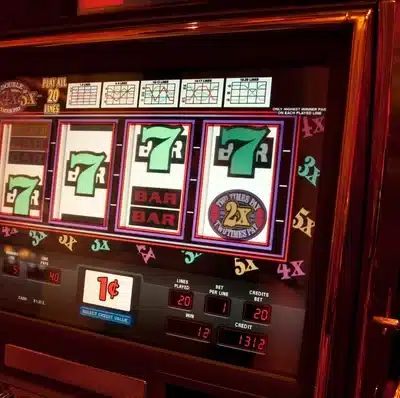 Kuvassa on peliautomaatti, jonka kirkkaasti valaistu näyttö esittää klassista kolikkopeliä. Ruudulla näkyy neljä rullaa, joista kolmessa on vihreä numero seitsemän ja yhdessä “BAR”-symboli sekä “2x”-kerroin. Pelin teema on perinteinen kasino-tyylinen, ja sen ympärillä loistaa lämmin, punertava valaistus, joka luo tunnelmallisen ja houkuttelevan ilmapiirin. Näytön alareunassa on tietoja panoksesta, voitoista ja krediiteistä, ja kolikoiden arvo on yksi sentti. Oikealla puolella näkyy metallinen pelivipu. Kuva välittää Las Vegas -tyylistä jännitystä ja pelaamisen odotuksen tunnetta.