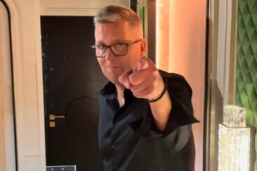 Jani Sievinen osoittaa sormella. Hänellä on päällään musta kauluspaita. Takana näkyy tumma ovi ja vaaleaa seinää.