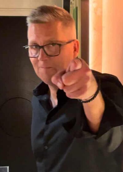 Jani Sievinen osoittaa sormella. Hänellä on päällään musta kauluspaita. Takana näkyy tumma ovi ja vaaleaa seinää.