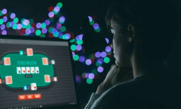 Pimeässä huoneessa on tietokoneen näyttö, jossa näkyy nettipokeripöytä. Tietokoneen edessä on nuori mies. Taustalla on valoja.