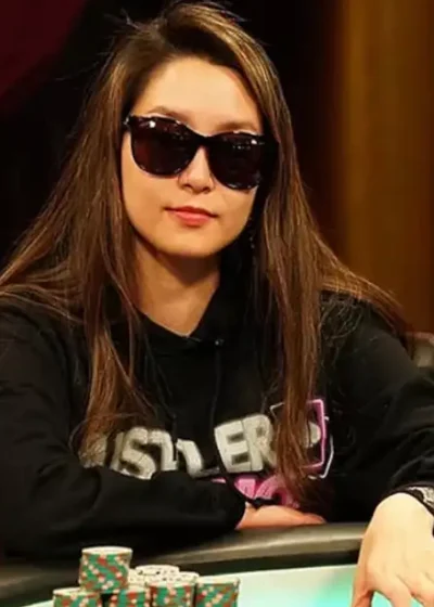 Nainen istuu pokeripöydässä. Hänellä on päällään musta huppari ja mustat aurinkolasit. Pokeripöydällä on paljon pelimerkkejä.