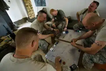 Viisi miestä pelaa pokeria pöydän ympärillä. Miehet ovat armeijassa ja heillä on päällään armeijan vaatteet.