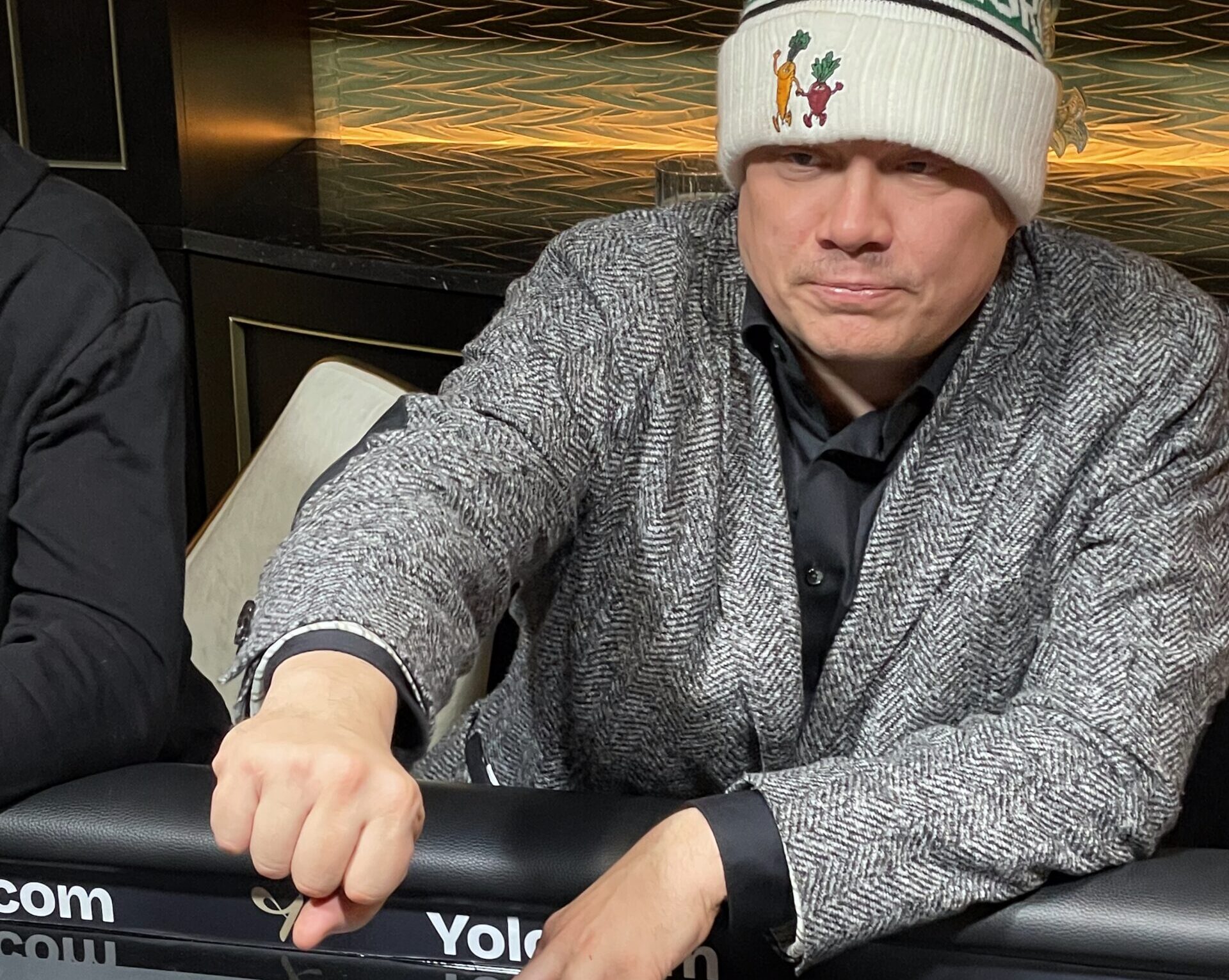 Ilari Sahamies istuu pokeripöydässä varastettu puvuntakki päällään ja Myrttisen suolakurkkujen pipo päässään