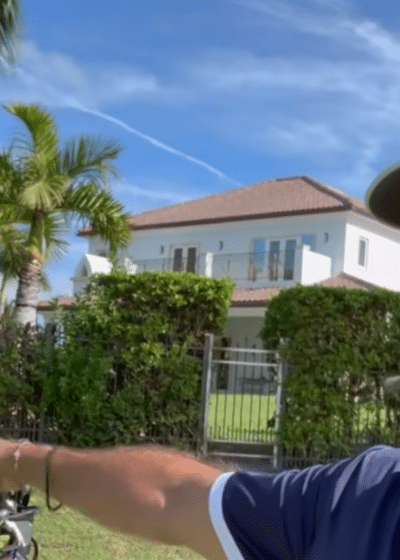 Kuvassa on kaksi miestä, molemmilla on valkoinen lippis. Toinen miehistä osoittaa toista sormella, taustalla näkyy sinistä taivasta ja palmupuita.