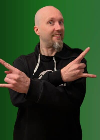 Markus Ylänne seisoo tumma huppari päällään. Hänellä on kädet ristissä edessään. Tausta on vihreän sävyinen.