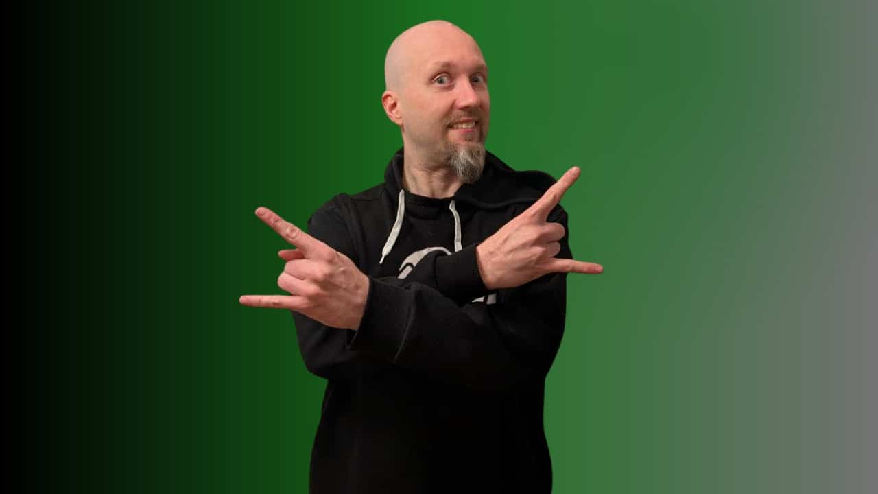 Markus Ylänne seisoo tumma huppari päällään. Hänellä on kädet ristissä edessään. Tausta on vihreän sävyinen.