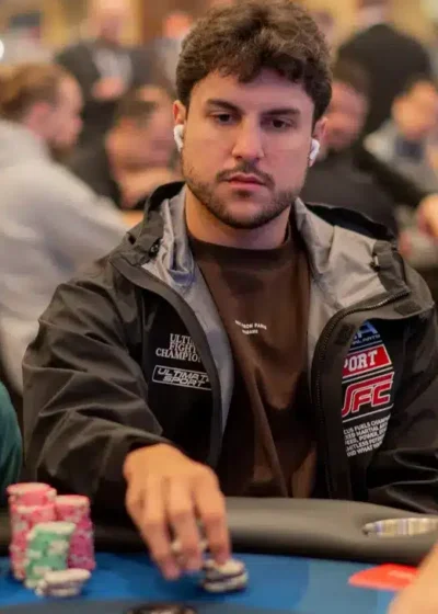 Kaksi miestä istuu pokeripöydässä. Pöydällä on erivärisiä pelimerkkejä. Toisella miehellä on aurinkolasit ja lippis päässä.