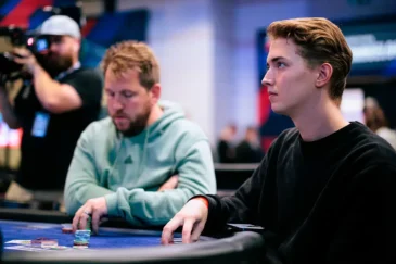 Luka Sorainen istumassa pelipöydässä vieressä vihreähupparinen mies ja takana kameramies