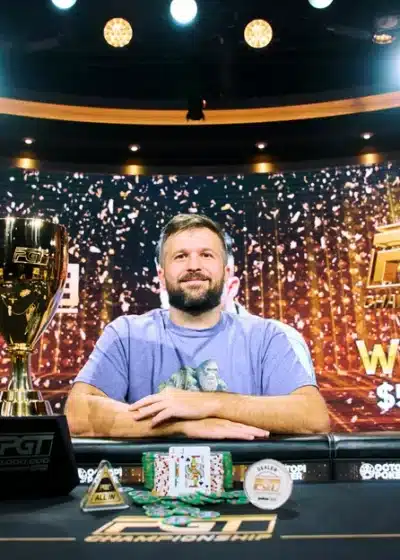 Mies sinisessä paidassa istuu pokeripöydän takana ja juhlii pokeriturnausvoittoaan.