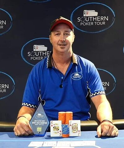 Mies sinisessä paidassa poseeraa voittajakuvassa pokeripöydän äärellä.