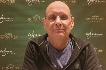 Kalju mies mustassa hupparissa poseeraa vihreää seinää vasten.