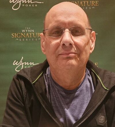 Kalju mies mustassa hupparissa poseeraa vihreää seinää vasten.