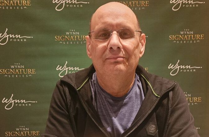 Kalju mies mustassa hupparissa poseeraa vihreää seinää vasten.