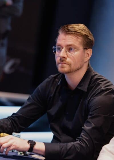 Mies tumman sinisessä kauluspaidassa istuu sinisen pokeripöydän äärellä