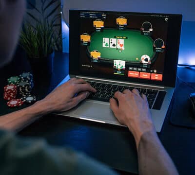 Mies pelaamassa nettipokeria tummssa huoneessa. Pöydällä on tietokone ja pelimerkkejä, sekä hiiri.