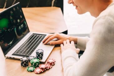 Kuvassa mies pelaa tietokoneella pokeria, vieressä hänellä on kasa pelimerkkejä.