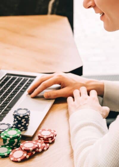 Kuvassa mies pelaa tietokoneella pokeria, vieressä hänellä on kasa pelimerkkejä.