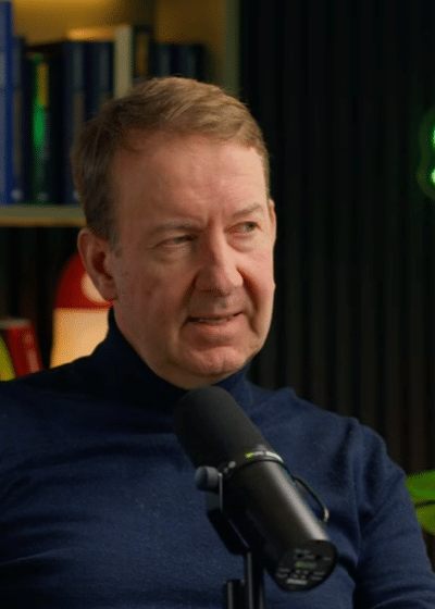 Mies istuu mikrofonin takana. Miehellä on päällään tummansininen paita ja taustalla olevalla seinällä on "STNX"-valokyltti