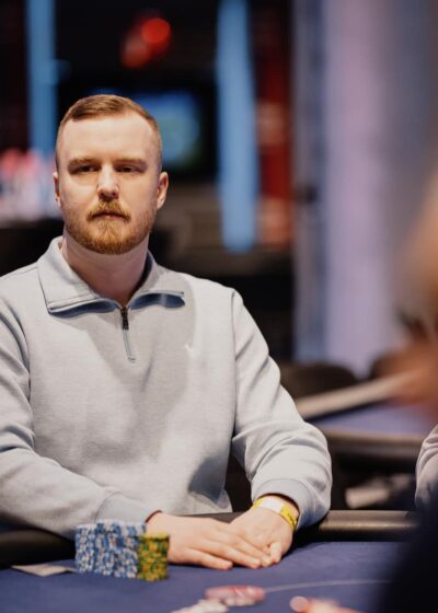 Mies harmaassa paidassa istuu sinisen pokeripöydän ääressä.
