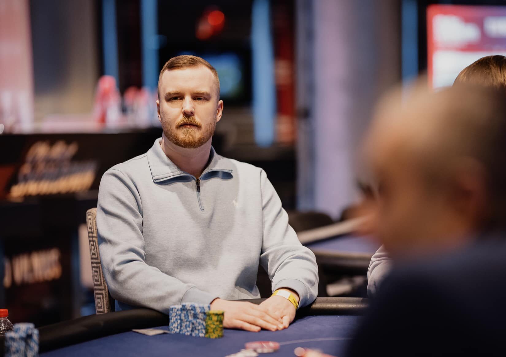 Mies harmaassa paidassa istuu sinisen pokeripöydän ääressä.