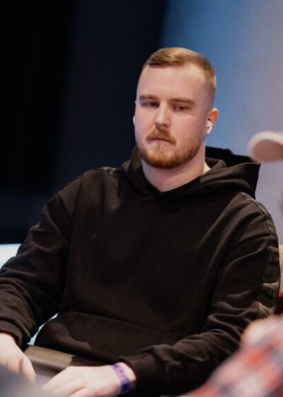 Mies mustassa hupparissa istuu pokeropöydän ääressä.