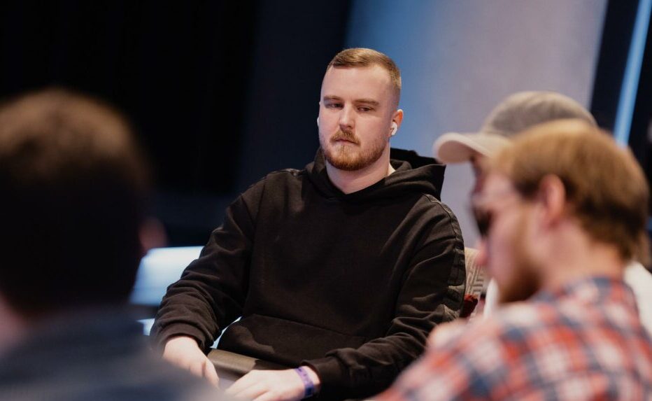 Mies mustassa hupparissa istuu pokeropöydän ääressä.