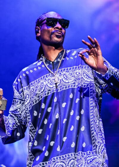 Kuvassa on artisti Snoop Dogg, jolla on päällään violetti kuvioitu paita.