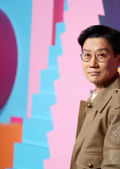 Mies vaaleanruskeassa takissa seisoo värikkään seinän edessä.