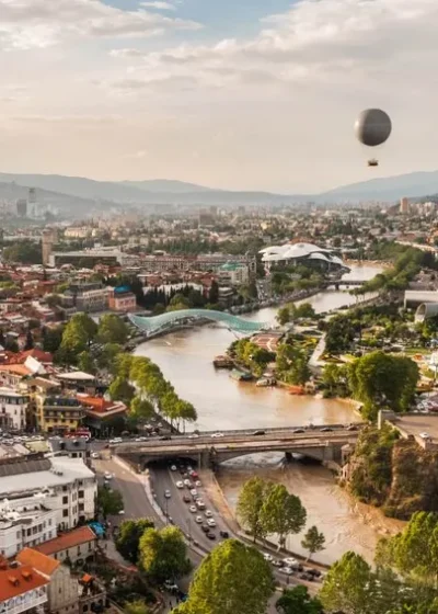 Ilmakuva Georgian Tbilisistä. Keskellä näkyy joki ja sen rannoilla on punakattoisia taloja.