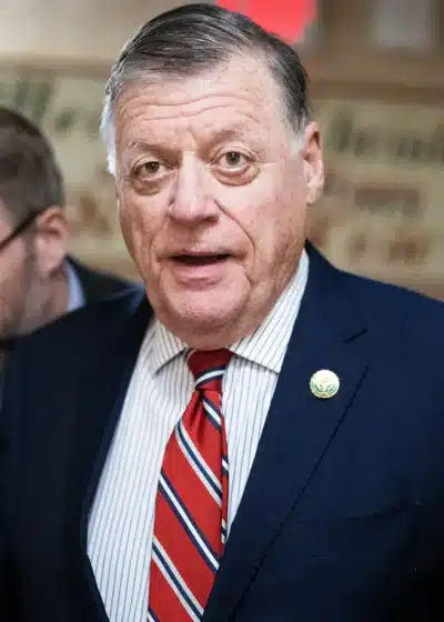 Kuvassa on vanha mies, jolla on päällään sininen puku ja punainen kravatti.