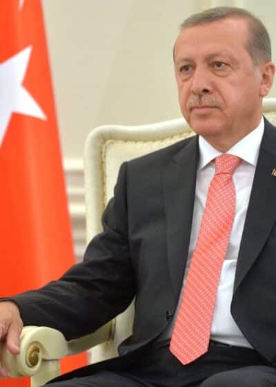 Turkin presidentti Erdogan istumassa puku päällä punaisen lipun vieressä, jossa tähti