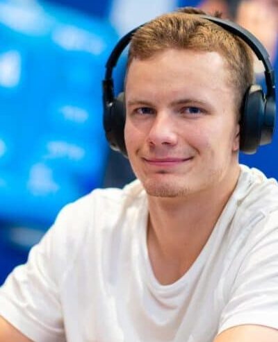 Miika Töyräs istuu pokeripöydässä. Hänellä on päässään mustat kuulokkeet ja päällään valkoinen t-paita. Tausta on sinistä.