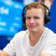 Miika Töyräs istuu pokeripöydässä. Hänellä on päässään mustat kuulokkeet ja päällään valkoinen t-paita. Tausta on sinistä.