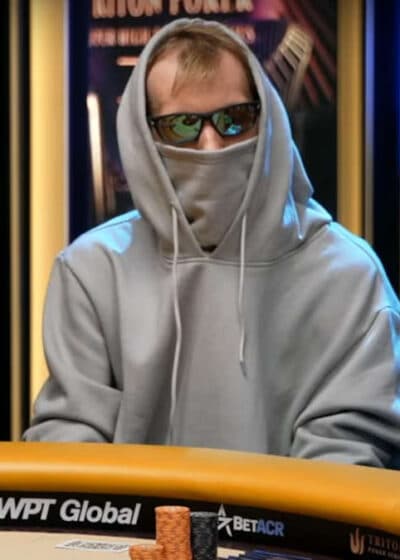 Harmaaseen huppariin ja aurinkolaseihin sonnustautunut mies istuu pokeripöydän ääressä.