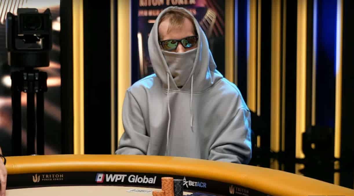 Harmaaseen huppariin ja aurinkolaseihin sonnustautunut mies istuu pokeripöydän ääressä.