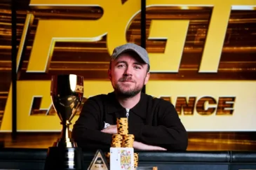 Patrick Leonard istuu pokeripöydässä. Hänellä on päällään musta paita ja lippis. Hänen edessään pöydällä on voittopokaali.