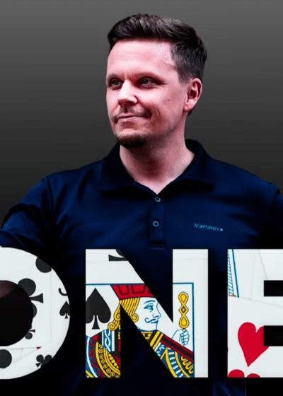 Miehellä on kädessään puhelin, joka on telineessä kiinni. Hänellä on tumman sininen paita, tausta on tumma