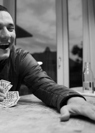 Kuva on väritön harmaa ja siinä esiintyy mies, joka istuu pöydässä ja hänellä on pelikortit kädessään.