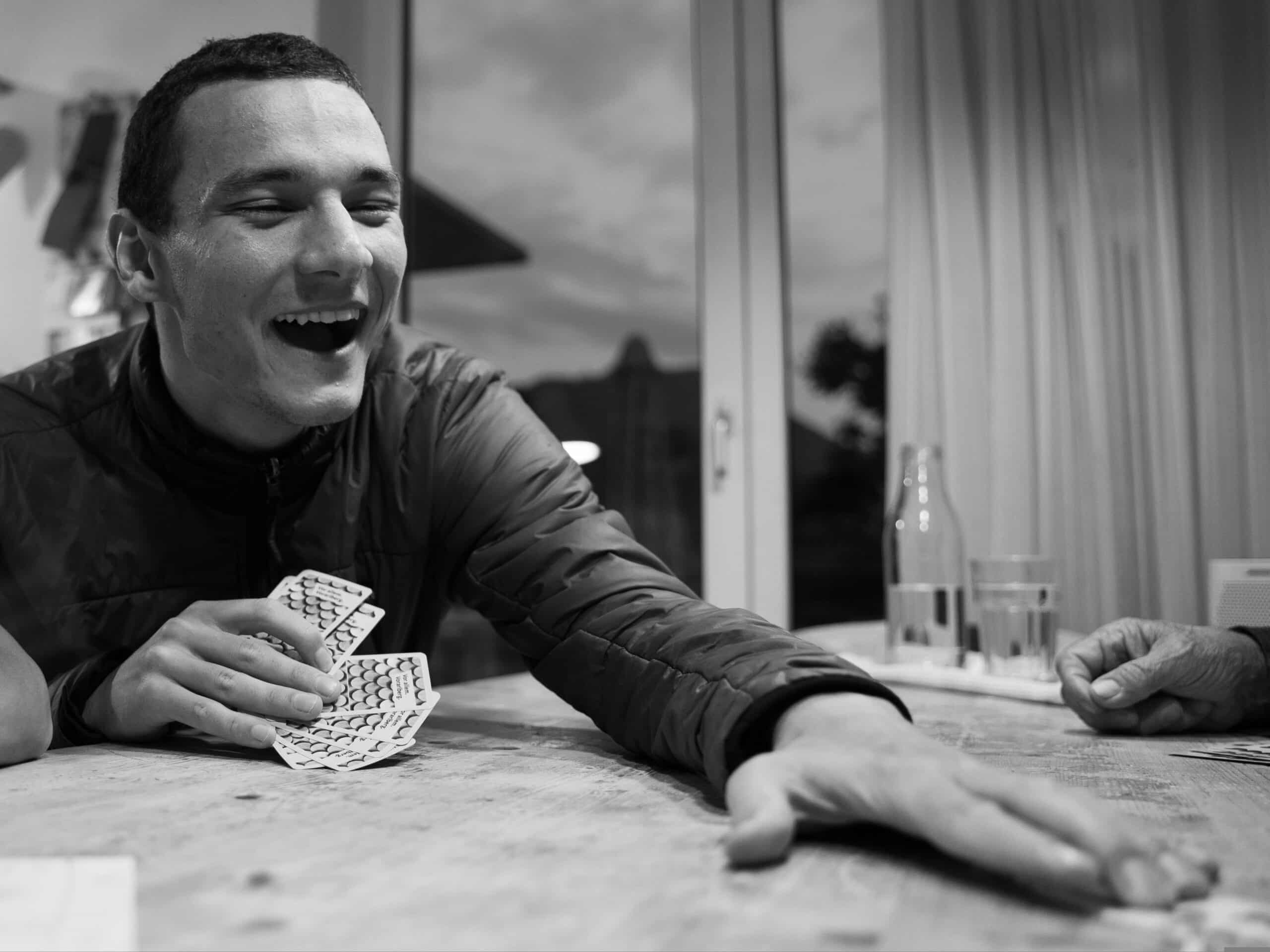 Kuva on väritön harmaa ja siinä esiintyy mies, joka istuu pöydässä ja hänellä on pelikortit kädessään.
