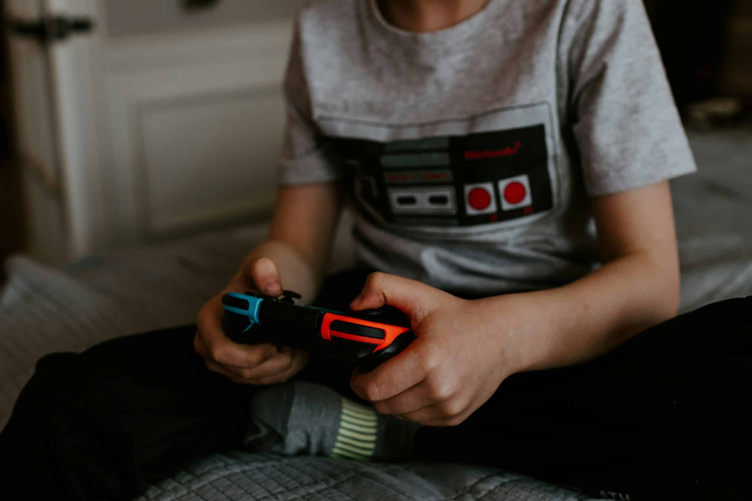 Kuvassa lapsi pelaa nintendo switch konsolilla jossa toinen puoli on sininen ja toinen punainen.