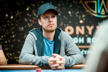 Joni Jouhkimainen istuu pokeripöydässä. Hänellä on päässään tumma lippis. Hänellä on kädet ristissä pöydän päällä.