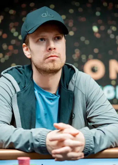 Joni Jouhkimainen istuu pokeripöydässä. Hänellä on päässään tumma lippis. Hänellä on kädet ristissä pöydän päällä.