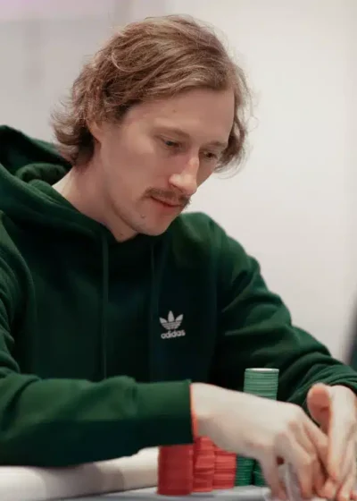 Aku Joentausta istuu pokeripöydässä. Hänellä on päällään vihreä huppari. Pöydällä Akun edessä on eri värisiä pelimerkkejä.