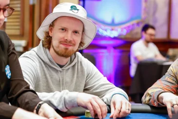 Joni Jouhkimainen istuu pokeripöydässä. Hänellä on päässään valkoinen lierihattu. Hänellä on kädet pöydällä ja käsissä on pelimerkkejä.