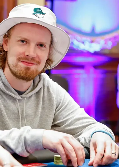 Joni Jouhkimainen istuu pokeripöydässä. Hänellä on päässään valkoinen lierihattu. Hänellä on kädet pöydällä ja käsissä on pelimerkkejä.