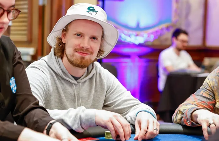 Joni Jouhkimainen istuu pokeripöydässä. Hänellä on päässään valkoinen lierihattu. Hänellä on kädet pöydällä ja käsissä on pelimerkkejä.