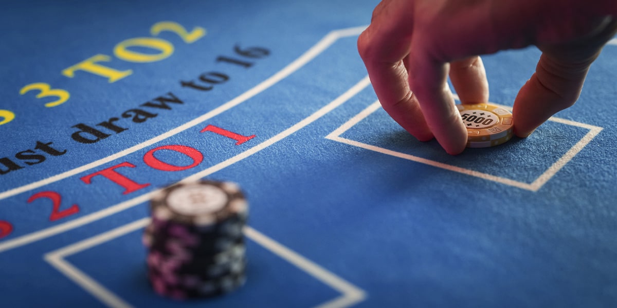 Kuvassa näkyy sinisellä kankaalla oleva Baccarat pöytä, jossa käsi asettaa pelimerkkejä.